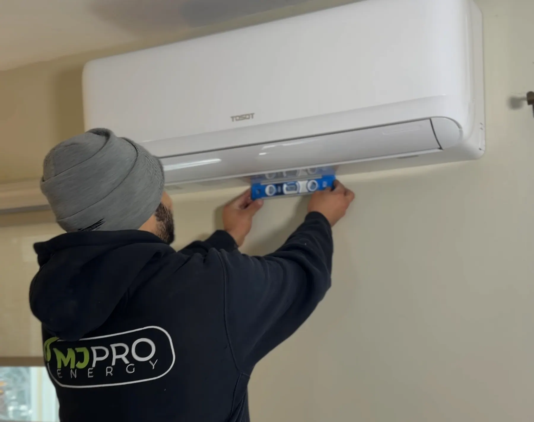 MJ Pro Energy technician leveling a Tosot mini split head on a wall